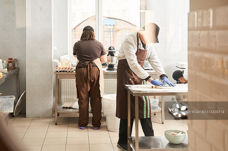男面包师在桌子上用擀面杖和面粉准备生面团图片素材