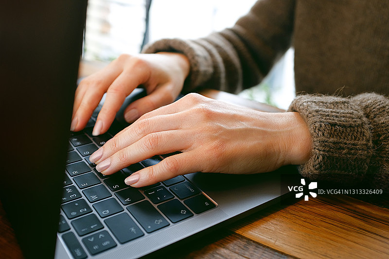 女人的手在电脑或笔记本电脑的键盘上打字。坐在办公桌前、共用办公区或咖啡馆里的上班族。商业、自由职业、在家工作的概念。通过社交网络、博客进行交流和认识。图片素材