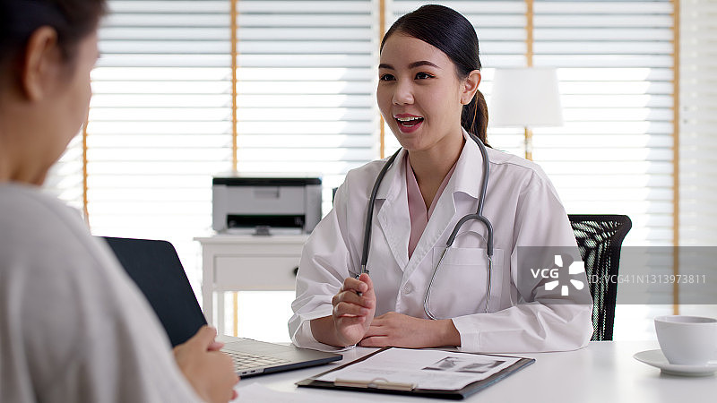 迷人的美丽年轻的亚洲医生女穿着白袍听诊器在肩上诊断与病人谈话提供帮助咨询，治疗或解释处方在办公室诊所。图片素材
