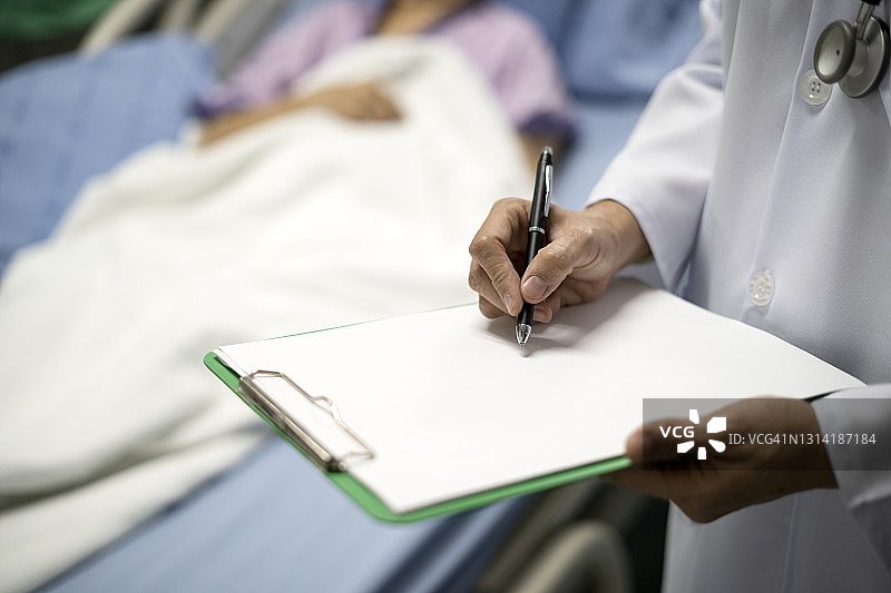 在医院病床上的医生访客和老年妇女的腹部。医生在医院用写字板为老年妇女写处方的照片。图片素材