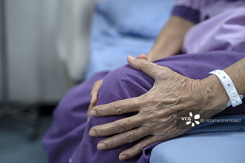 健康问题概念:在医院等待医生检查期间，一位面目全非的老年妇女坐在床上的剪发照片。图片素材