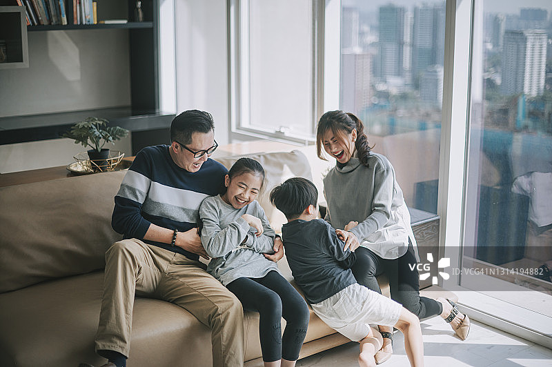 亚洲华人父母和他们的孩子在家里的客厅里在沙发上互相依偎着玩图片素材