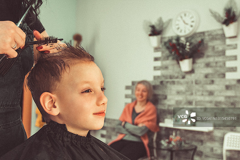开朗的小男孩在美发店做时髦的发型。为孩子理发和梳头图片素材