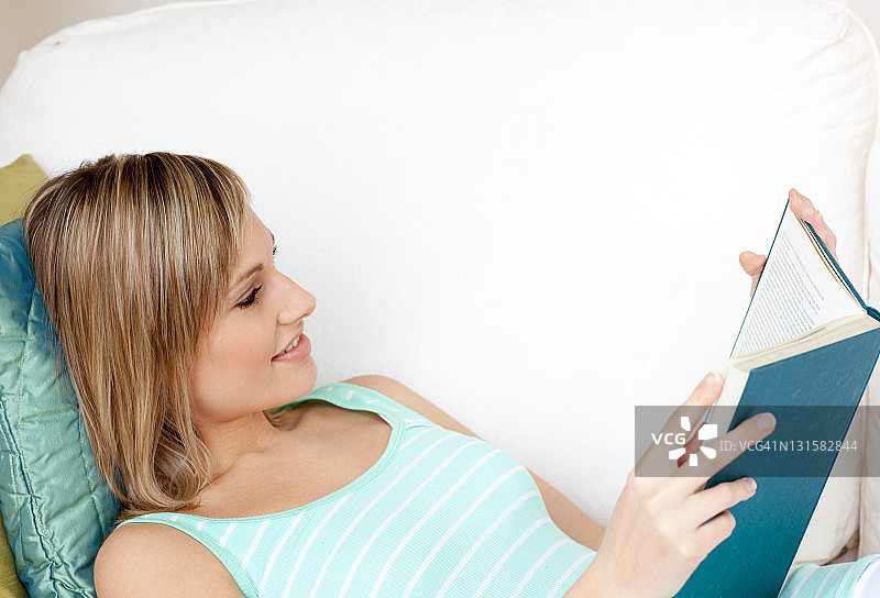 容光焕发的女人躺在沙发上看书图片素材