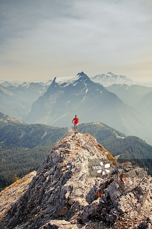 身穿红衫的徒步者站在山顶上，身后是风景如画的风景图片素材