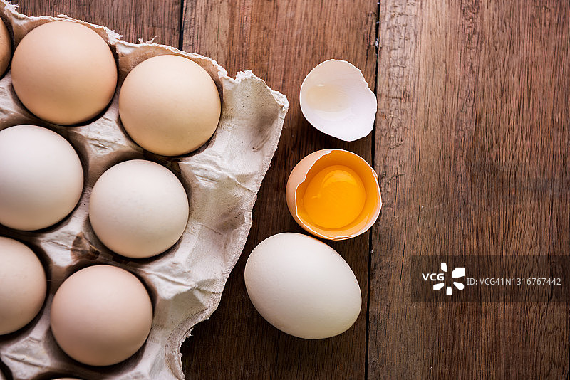 新鲜的鸡蛋在一个木制的乡村背景，新鲜的破蛋黄图片素材