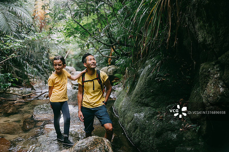 父亲和女儿徒步通过河流的丛林，冲绳，日本图片素材