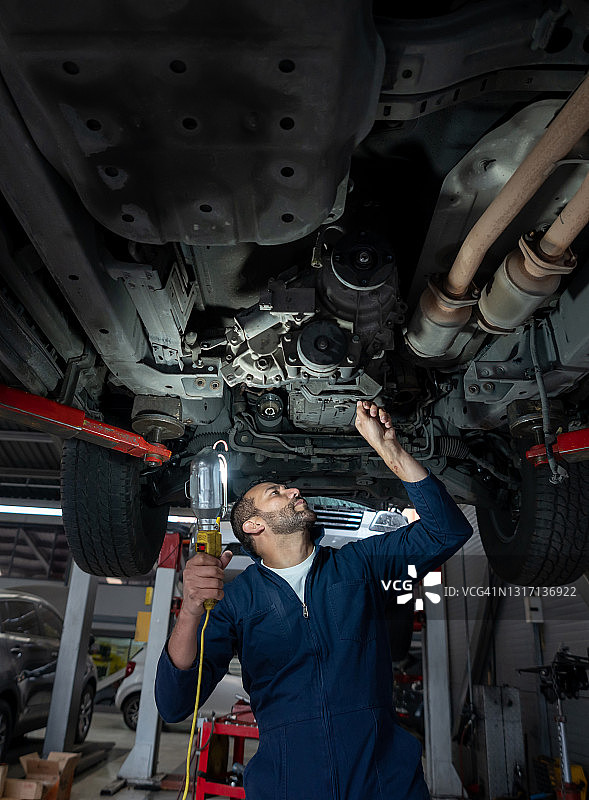 汽车修理工在汽车修理厂工作，在电梯上修理汽车并使用一盏灯图片素材