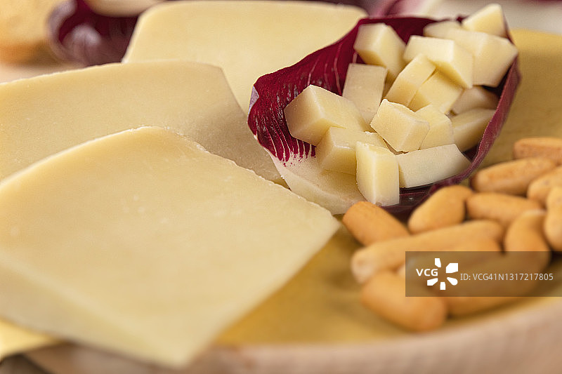 这是一张典型的意大利浅色奶酪的细节照片，放在一个木制砧板上，然后切成小块放在沙拉叶子里。高清晰度图像，为杂志，社交网络，网站和广告图片素材