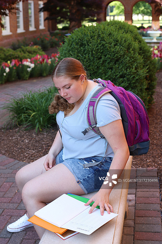 14岁的女孩阅读为回学校摆姿势与她的笔记本和背包。图片素材