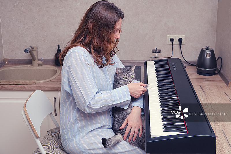 一个女人在家里的厨房里学习弹钢琴，旁边是一只猫图片素材