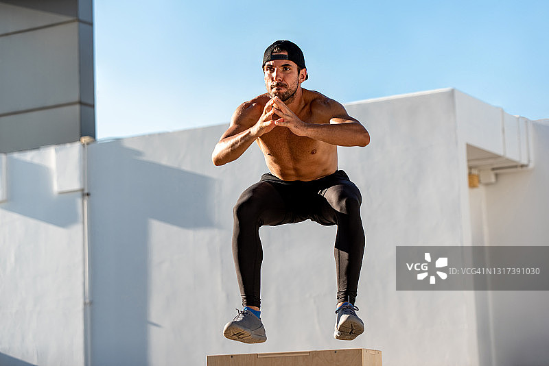 健美赤膊运动员跃上增强式木箱户外建筑屋顶，家庭锻炼运动概念图片素材