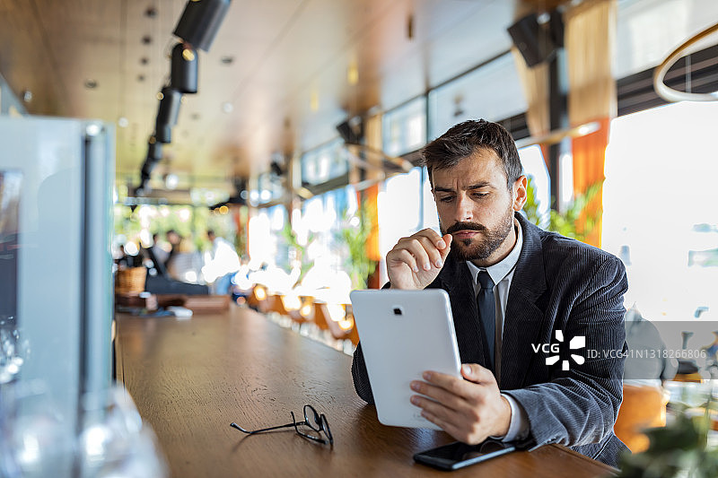 年轻的商人穿着商务套装正在城市餐厅放松和工作在他的数字平板电脑。图片素材