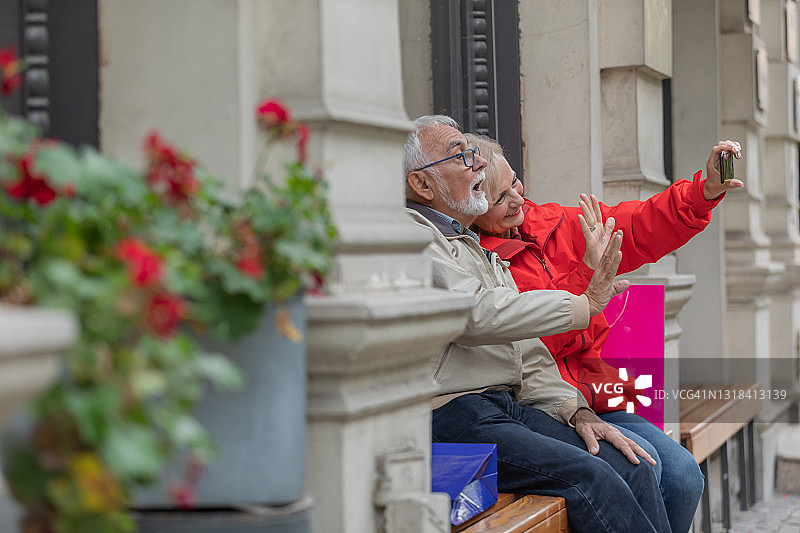 一个快乐的老夫妇的肖像在爱谁是坐在木凳上和拍自己的照片。图片素材