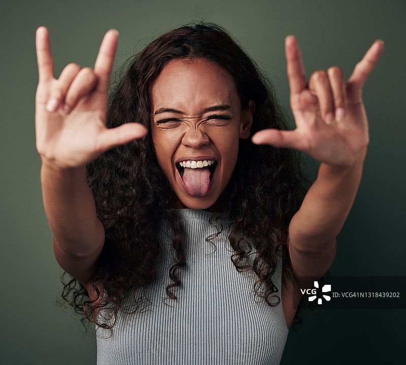 摄影棚拍摄了一个年轻女子在一个绿色背景下做一个摇滚手势图片素材