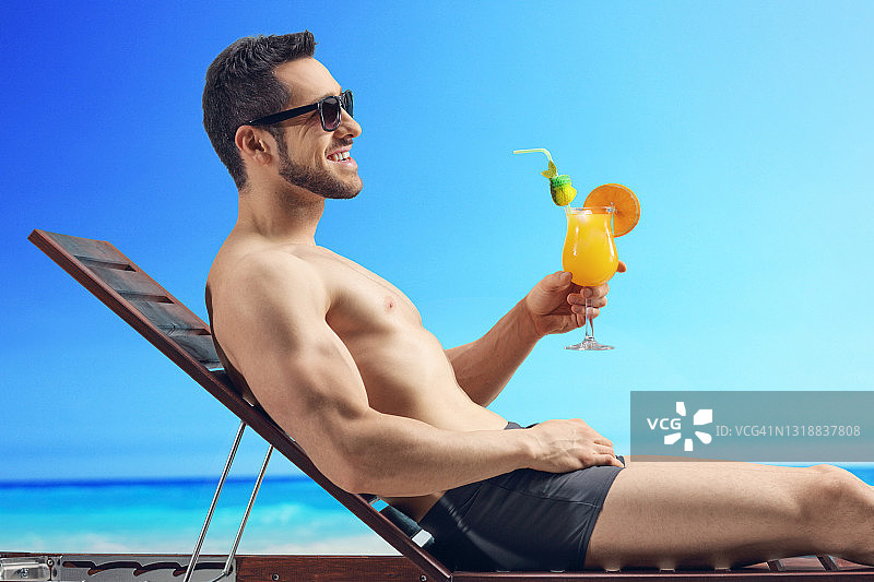 一个男人在海边的海滩上晒着太阳，拿着一杯鸡尾酒图片素材