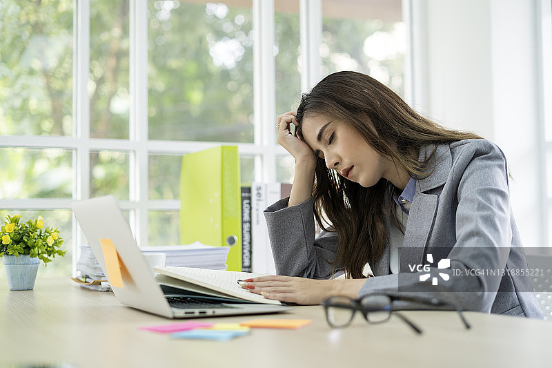 这是一个年轻的女商人在现代办公室使用笔记本电脑时头疼的照片。图片素材