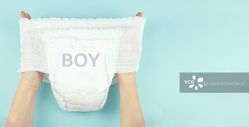 手上的婴儿尿片上刻着“男孩”字样，背景为蓝色。空间的文本图片素材