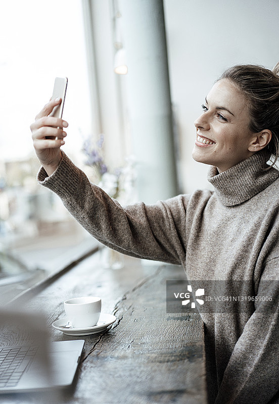 微笑的女顾客在咖啡厅用手机自拍图片素材