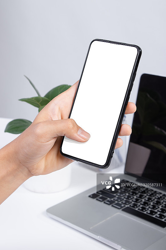 一个智能手机空白屏幕模拟出现在白色的办公桌上。图片素材