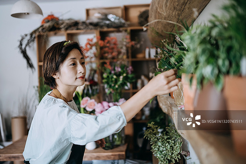 年轻的亚洲女花商，小生意花店的老板，处理和照顾新鲜的鲜花和植物在工作场所。喜欢和花在一起的工作。中小企业的概念图片素材