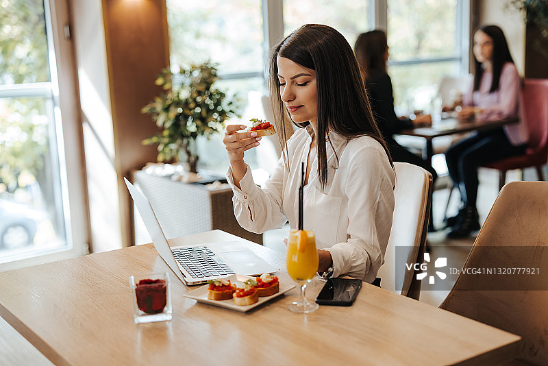 年轻女子在餐厅吃早餐时使用笔记本电脑图片素材