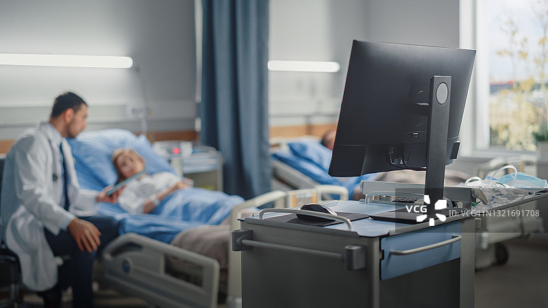 医院病房:现代先进高科技医疗计算机。在现代设备的背景下，临床外科医生使用平板电脑在床上咨询手术成功后恢复的患者图片素材