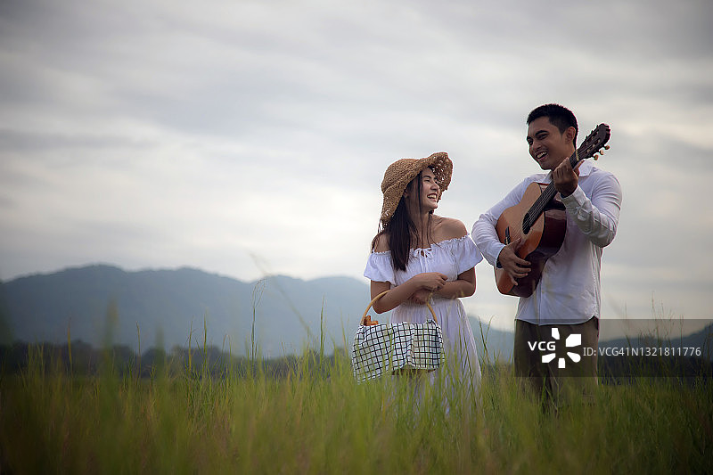年轻的亚洲夫妇放松与吉他在广阔的草地上度假。图片素材