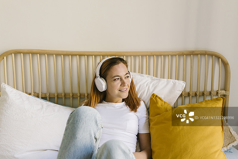 微笑的女人通过耳机听音乐在床上在家图片素材