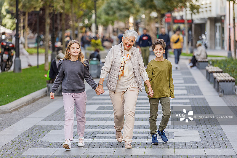 一位老妇人和她的孙子孙女走在城市的街道上。图片素材