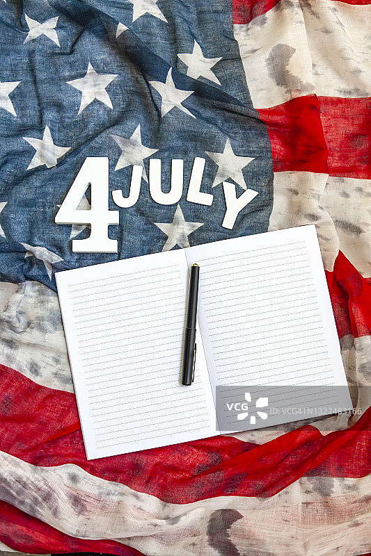 俯视图“7月4日”由数字和白色木制字母、空白记事本、眼镜和黑色铅笔组成的美国国旗。7月4日，独立日。图片素材