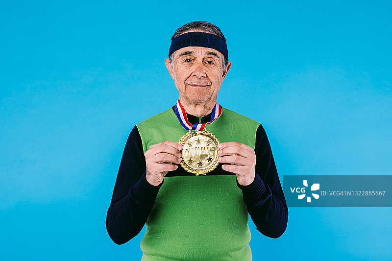 年长的运动员在绿色和黑色的复古球衣，与一个大的胜利者奖牌显示它，在蓝色的背景。图片素材