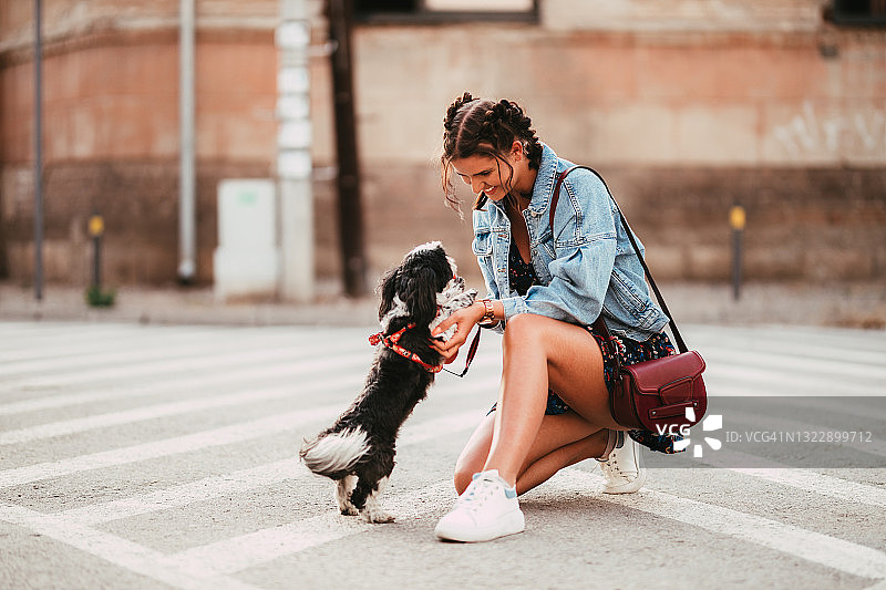 一个年轻女子在城市的街道上和一只狗玩耍图片素材