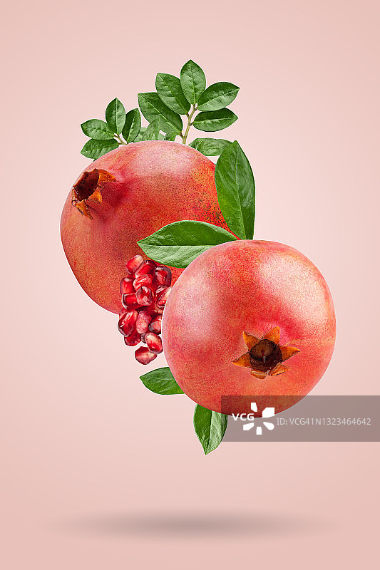 一个成熟的石榴，种子和叶子在空中飞舞在粉红色的背景。背景以石榴果。图片素材