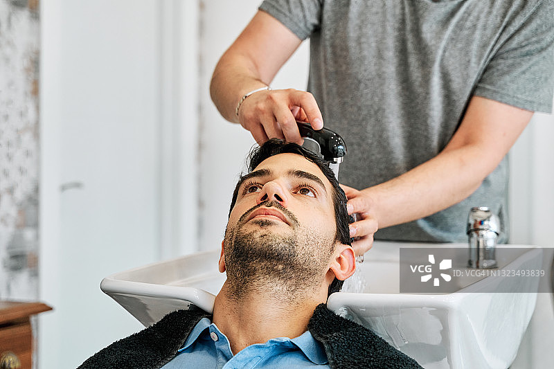 前面的观点，一个不认识的理发师洗一个年轻人的头发之前给他理发在理发店。图片素材