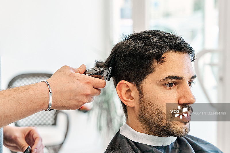 理发师在一家理发店里用理发器给一个年轻人理发。图片素材