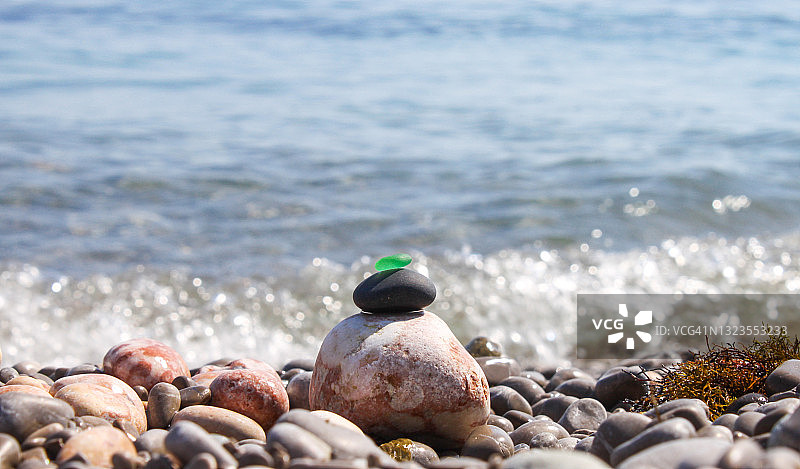 金字塔建在由海卵石组成的卵石海滩上，顶部是磨砂光滑的绿色玻璃。在波浪的背景下，水溅起了水花和泡沫图片素材