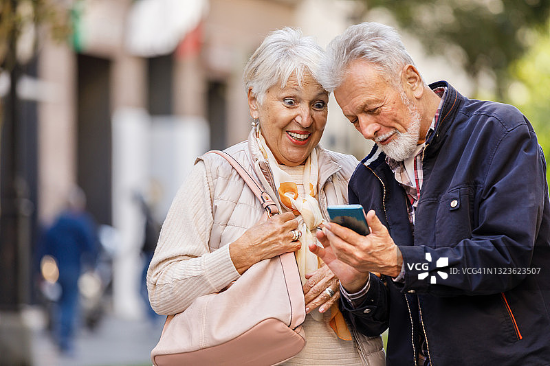 一对老年情侣在市区散步，享受一个秋天的下午，看手机。图片素材