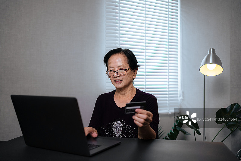 亚洲高级女性在笔记本电脑上使用信用卡进行网上银行。图片素材