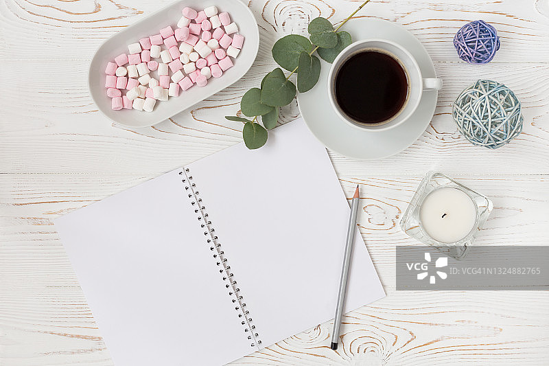 早餐用的咖啡杯，粉红色的棉花糖和空白笔记本，铅笔，白色桌上的花。女人的办公桌。图片素材