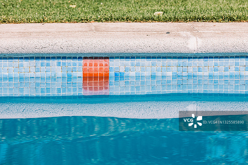 泳池边缘的细节与蓝色瓷砖和红色条纹表示深的区域，在一个阳光明媚的夏天图片素材