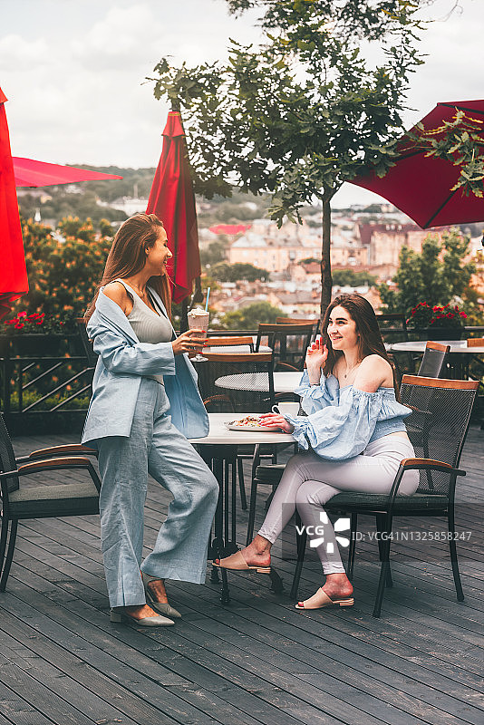 两个年轻的女性朋友在咖啡馆吃早餐，讨论着新闻，笑着。女性在咖啡馆喝鸡尾酒。图片素材