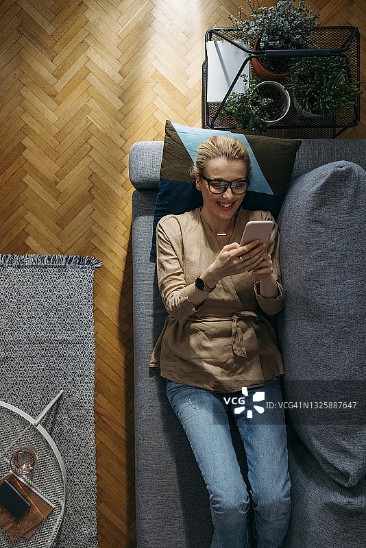 俯视图快乐的女人在家里的沙发上使用手机图片素材