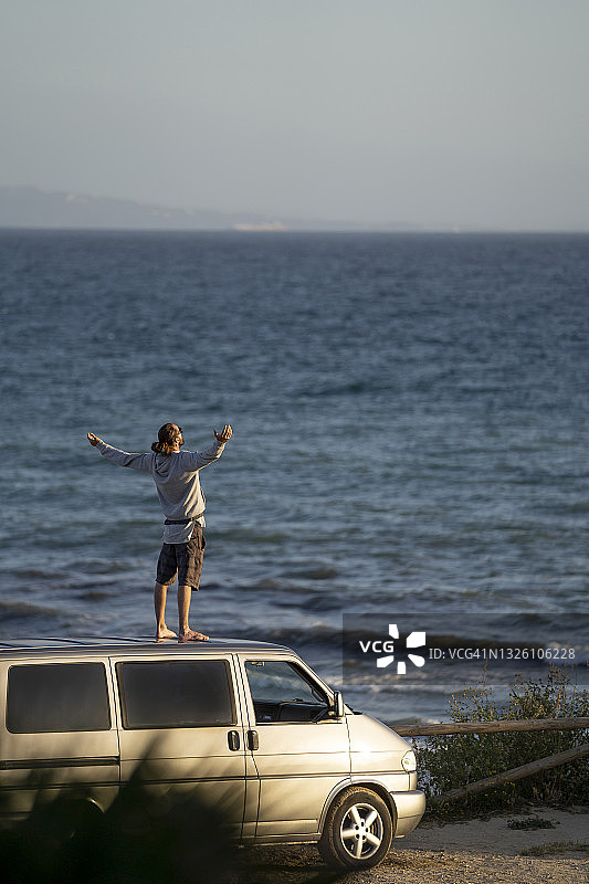 一个年轻人张开双臂站在海上的货车顶上图片素材