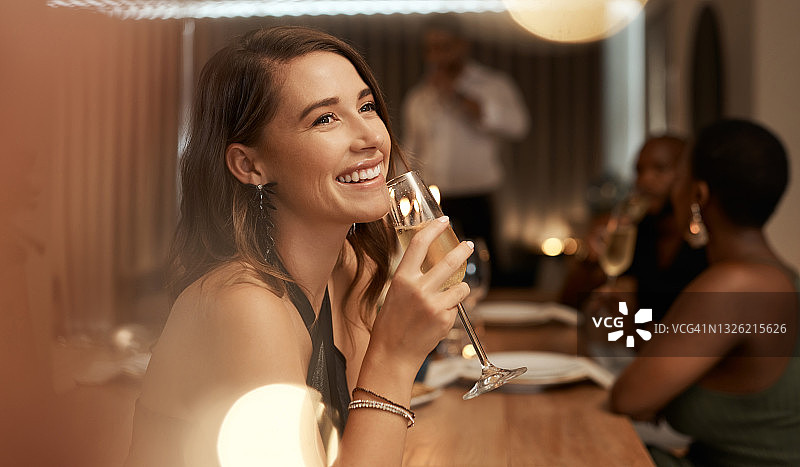 一个迷人的年轻女子坐在她的朋友在一个晚宴上，享受一杯香槟图片素材