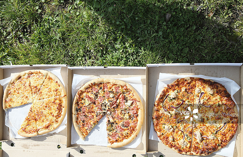 带走的食物。绿色草地上的手工盒子里的什锦披萨图片素材