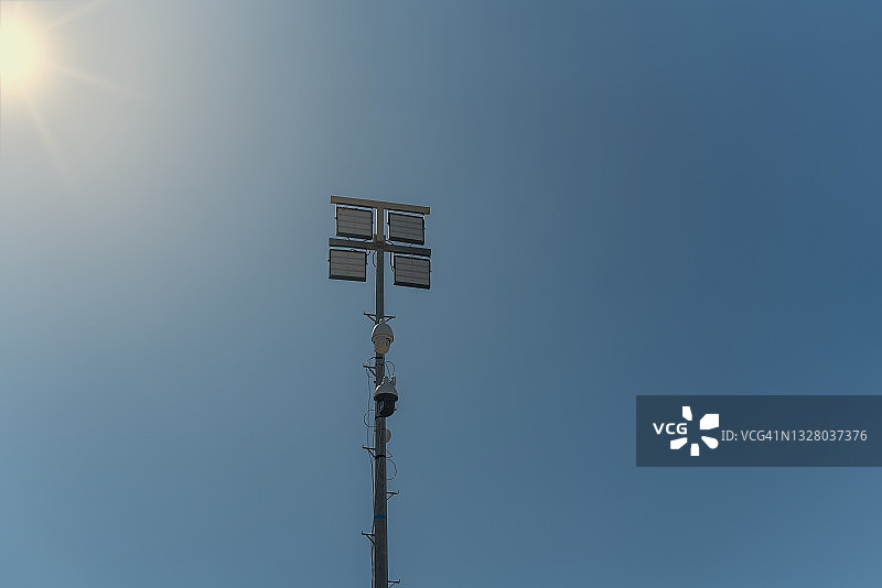 一根有监控摄像头的杆子，在犯罪区，还有夜间照明灯。映衬着蓝天和太阳。图片素材