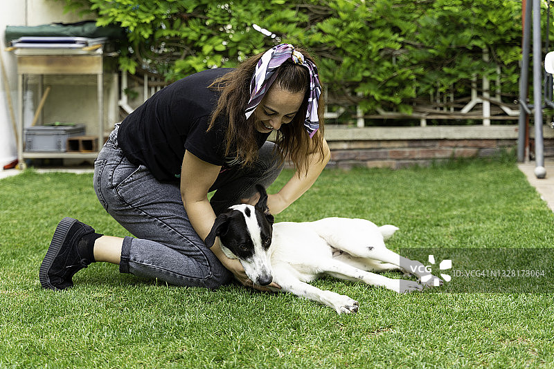 快乐的年轻女人和她的狗在公园草地上玩图片素材