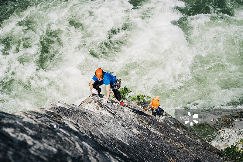 一位男性攀岩者攀登一个戏剧性的岩面高耸在威斯勒附近汹涌的河流之上，BC图片素材