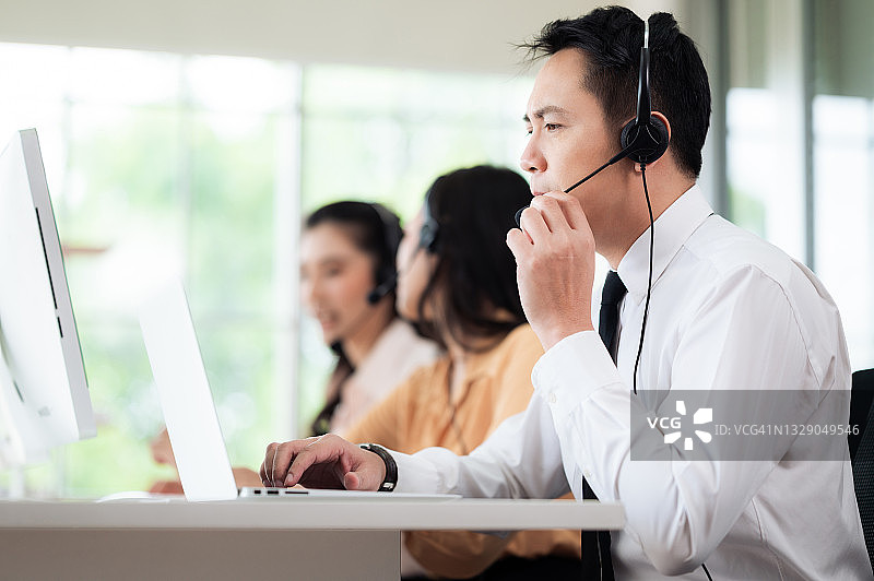 亚洲呼叫中心的工作人员戴着耳机和麦克风。在办公桌和电脑前为客户服务时感到压力和头痛。服务理念与咨询。通信的概念。图片素材